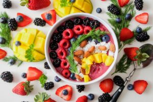 A bowl filled with a variety of fresh fruit and berries, accompanied by a spoon for serving.