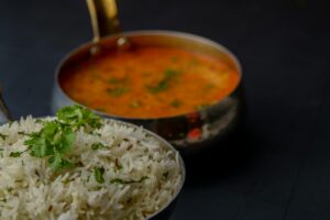 A bowl of rice accompanied by a spoon resting beside a small dish of sauce, ready for serving.