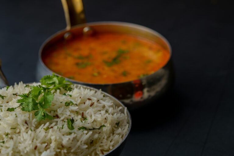 A bowl of rice accompanied by a spoon resting beside a small dish of sauce, ready for serving.