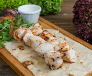 Grilled chicken kebabs displayed on a wooden cutting board, featuring colorful vegetables and juicy meat pieces.