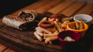 A plate featuring golden fries, a wrapped burrito, and a small cup of ketchup for dipping.