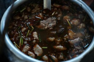 A steaming pot of soup with a silver spoon placed inside, indicating a hearty dish prepared for enjoyment.