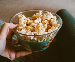 A hand holding a bowl of popcorn, ideal for snacking during a film.
