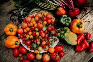  A colorful assortment of vegetables on a table, featuring a prominent plate of ripe tomatoes