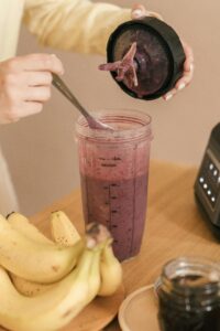 A woman is pouring a vibrant smoothie into a blender, surrounded by fresh fruits on a kitchen countertop